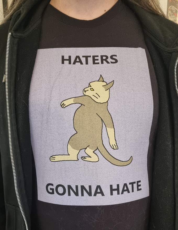 A person wears a t-shirt of a chill cat surrounded by "HATERS GONNA HATE"