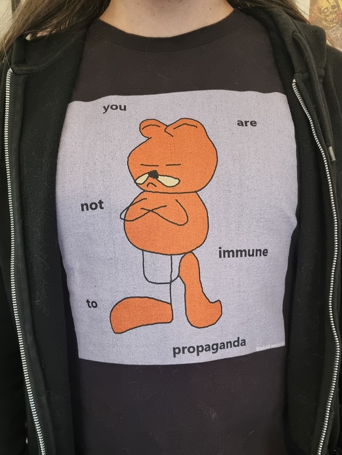 A person wears a t-shirt of Garfield surrounded by text bits "you are not immune to propaganda"